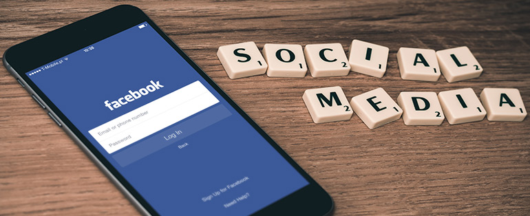 Smartphone com o login do Facebook na tela. Ao lado, peças do jogo "Palavra Cruzada" formando a palavra Social Media. 