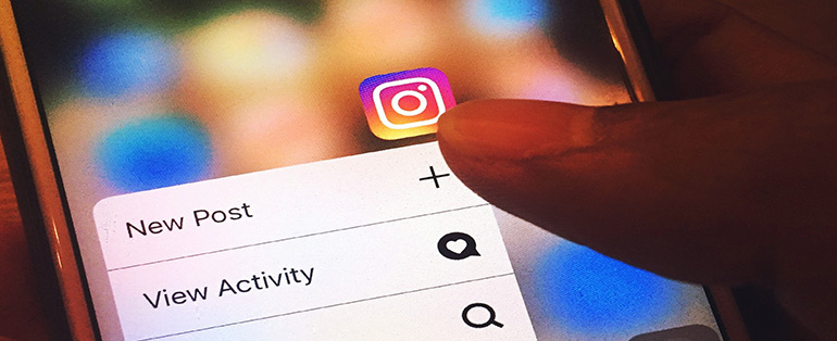 Zoom de dedo tocando um smartphone. Na tela, o ícone do Instagram com as opções "New Post" e "View Activity".